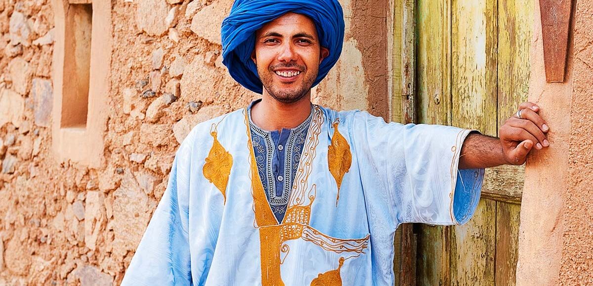 Moroccan Berber man with Berber outfit smiling in front of an old house door at a Berber Village.