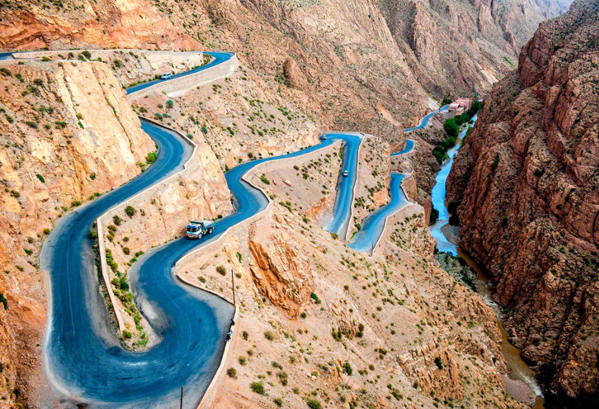 Serpentine mountain road winding through the Dades Gorges in Morocco with a river running alongside.