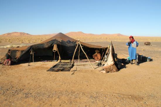 Nomadic Berber next to a traditional tent in the Moroccan desert landscape.