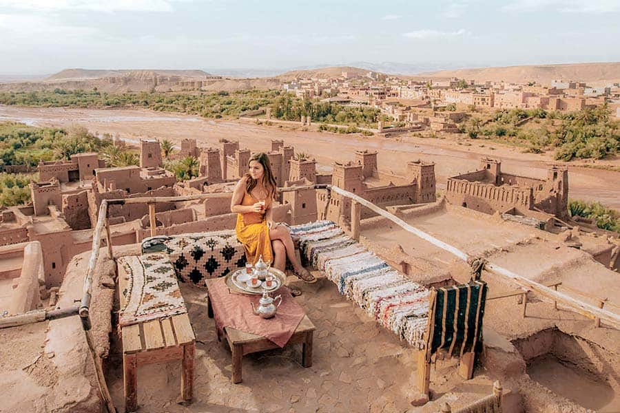 Woman in yellow sitting atop Kasbah Ait Ben Haddou overlooking the village