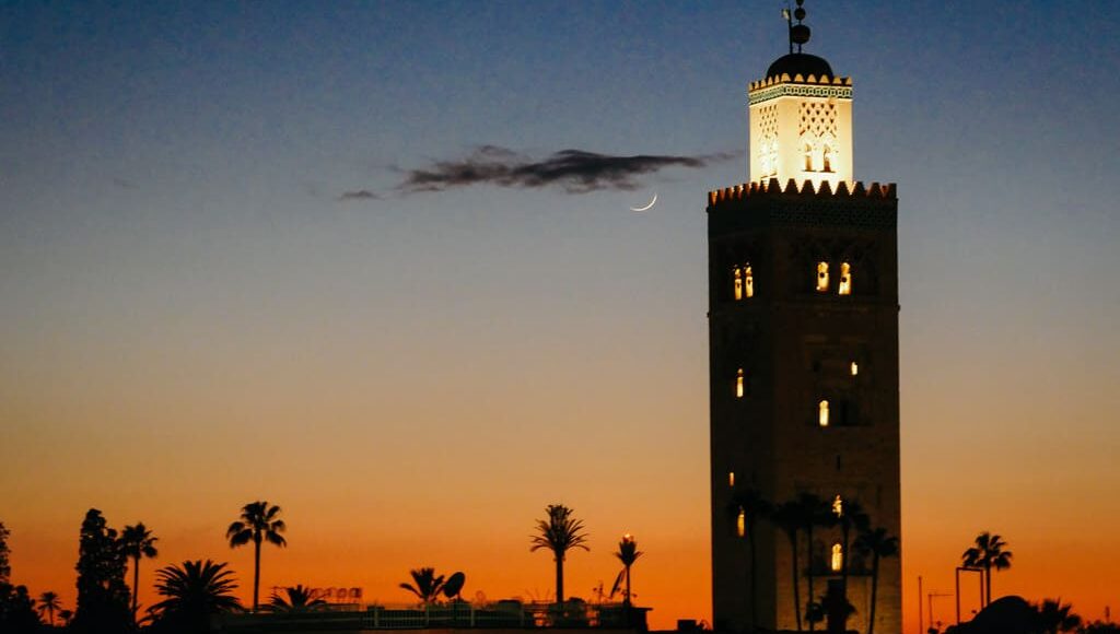 Silhouette of Koutoubia Mosque's minaret against a twilight sky with a crescent moon during Ramadan in Marrakech, Morocco.