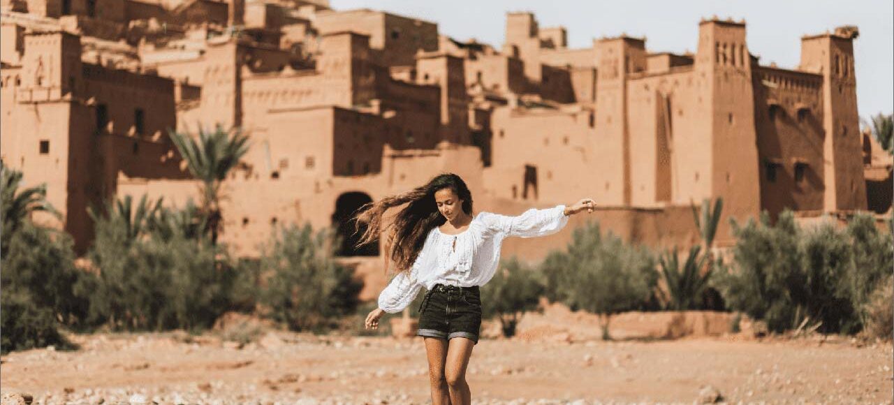 Woman with flowing hair joyfully running in front of Kasbah Ait Ben Haddou