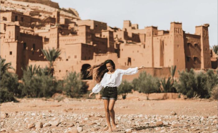 Woman with flowing hair joyfully running in front of Kasbah Ait Ben Haddou