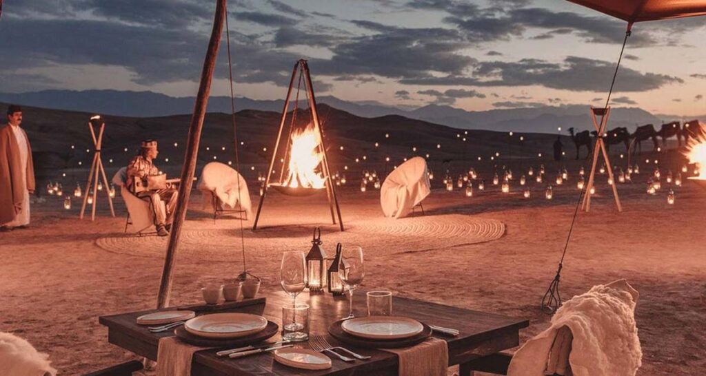 Luxury outdoor dining setup in the Agafay Desert with a bonfire and lanterns at twilight.