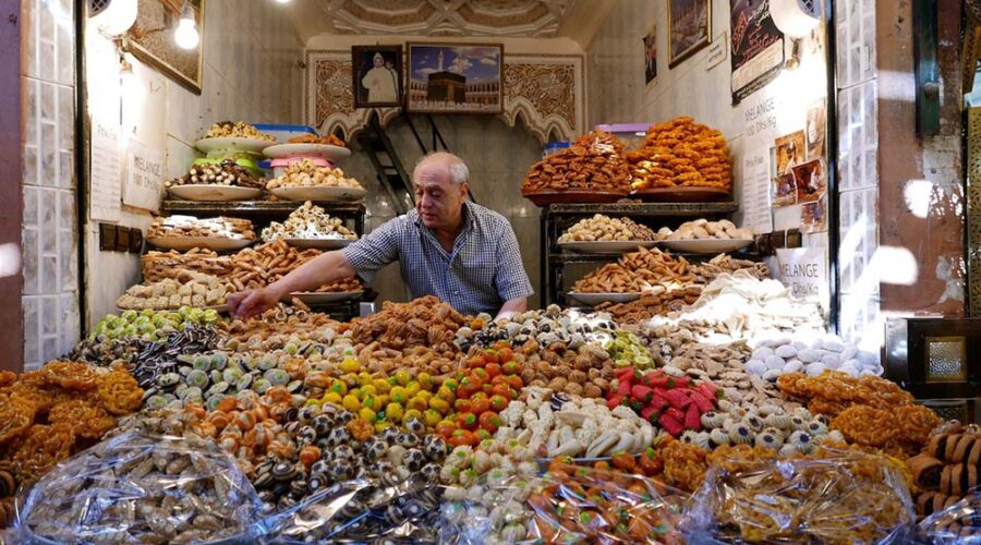 Vendor arranging an abundant display of traditional Moroccan pastries at a stall in Marrakech Medina.