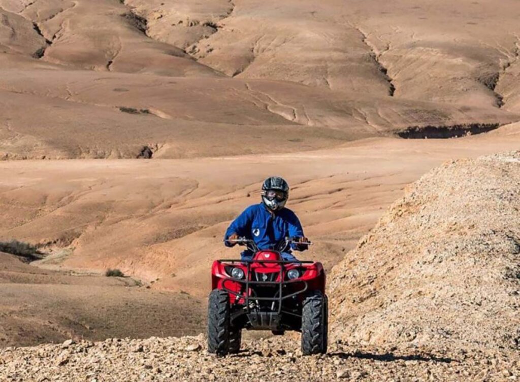 Adventurer riding a red quad bike in the rugged terrain of the Agafay Desert.
