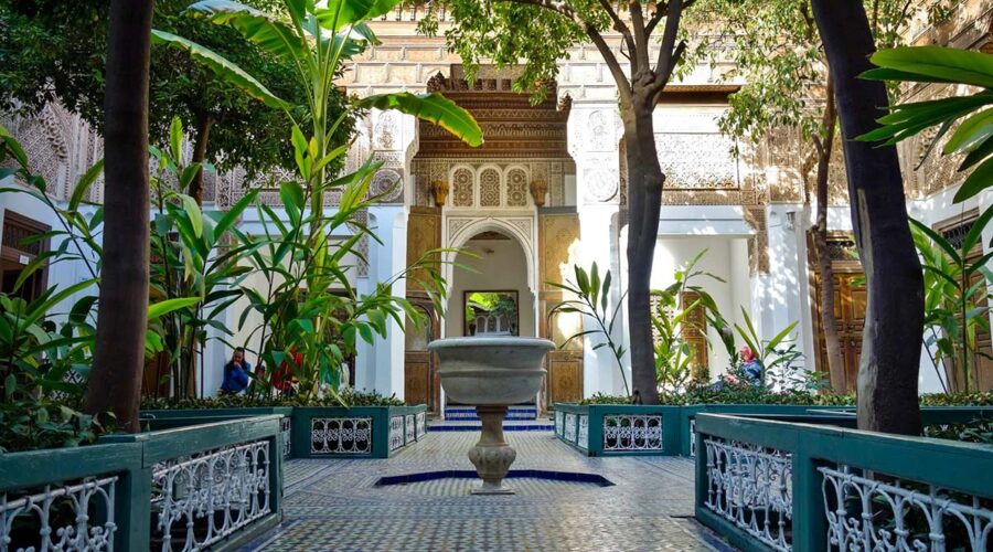 Serene courtyard of Bahia Palace in Marrakech, with ornate arches, traditional tiles, and a central marble fountain.