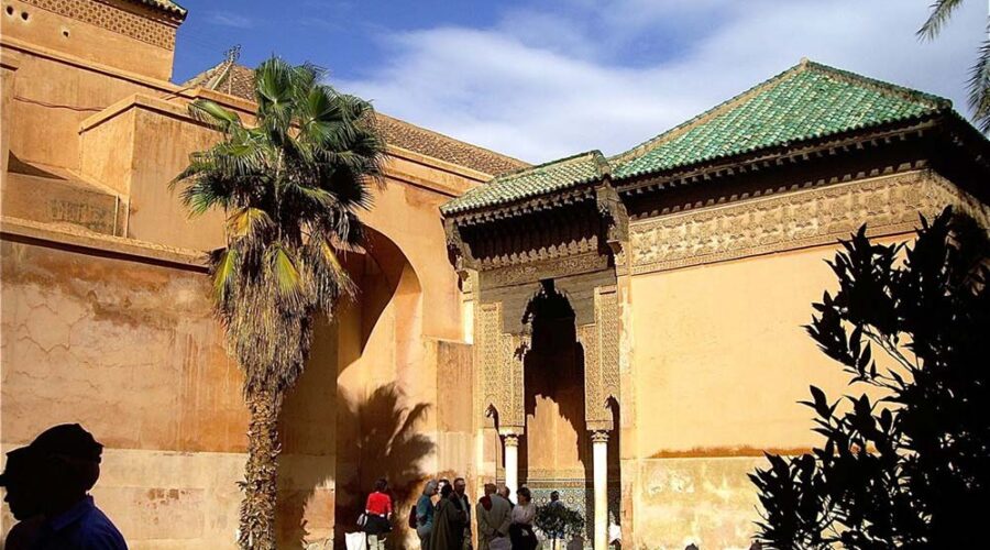 Tourists exploring the historic Saadian Tombs surrounded by ancient walls and palm trees in Marrakech's Medina.