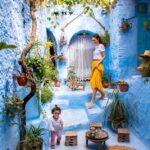 Mother and child enjoying a vibrant alley in Chefchaouen, with blue walls and plant pots, capturing a joyful moment.