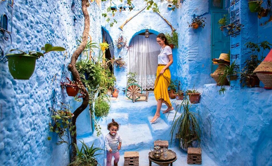 Mother and child enjoying a vibrant alley in Chefchaouen, with blue walls and plant pots, capturing a joyful moment.