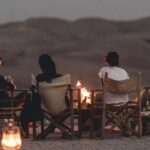 Four friends enjoy a candlelit dinner in the Agafay Desert, with rolling dunes under a twilight sky.