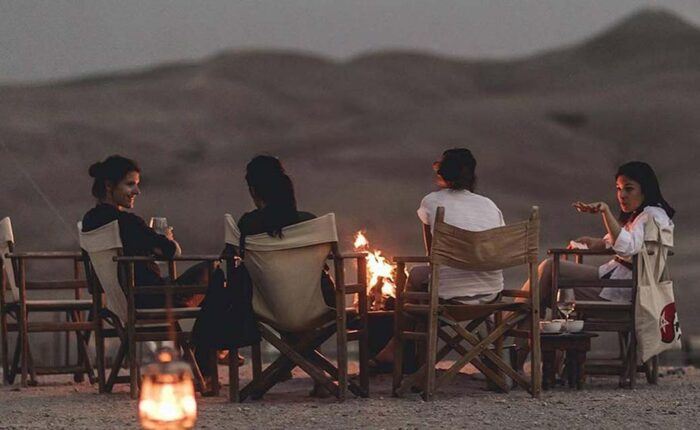 Four friends enjoy a candlelit dinner in the Agafay Desert, with rolling dunes under a twilight sky.