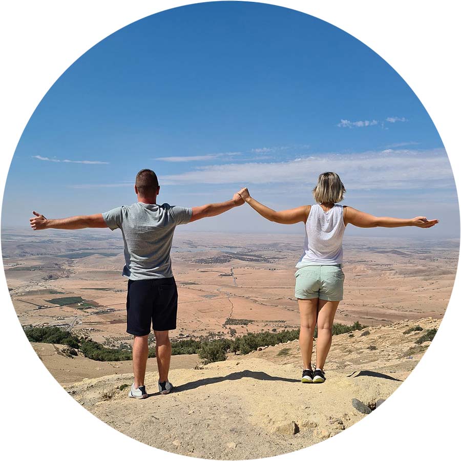 Two adventurers holding hands, arms outstretched, overlooking a vast desert landscape.