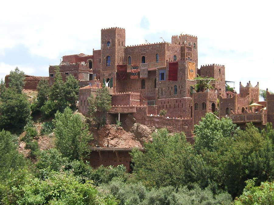 Ancient red clay Berber castle nestled in the greenery of the Ourika Valley, under the clear Moroccan sky.