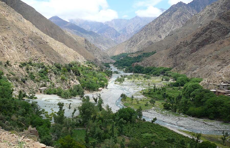 Meandering river in Ourika Valley with lush greenery and towering Atlas Mountains.