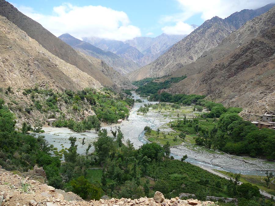 Meandering river in Ourika Valley with lush greenery and towering Atlas Mountains.