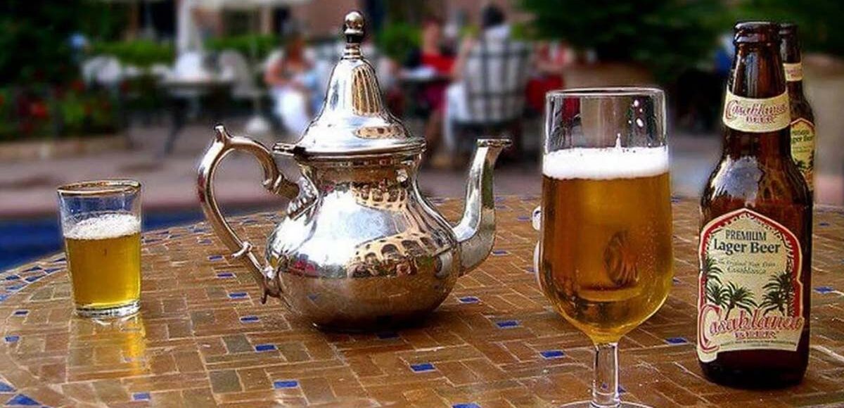 Casablanca beer bottle next to a full glass and traditional Moroccan tea set on a mosaic table.