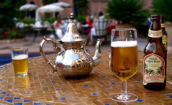 Casablanca beer bottle next to a full glass and traditional Moroccan tea set on a mosaic table.
