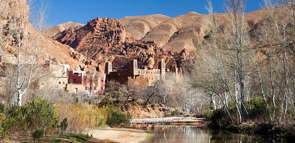 Scenic view of a river, historic Kasbah, and unique rock formations in Dades Valley, Morocco.
