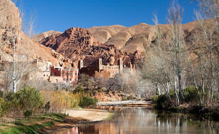 Scenic view of a river, historic Kasbah, and unique rock formations in Dades Valley, Morocco.