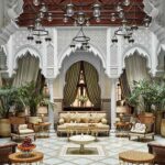 Luxurious Moroccan riad interior showcasing classical architecture with carved archways, opulent chandeliers, and a central garden area.