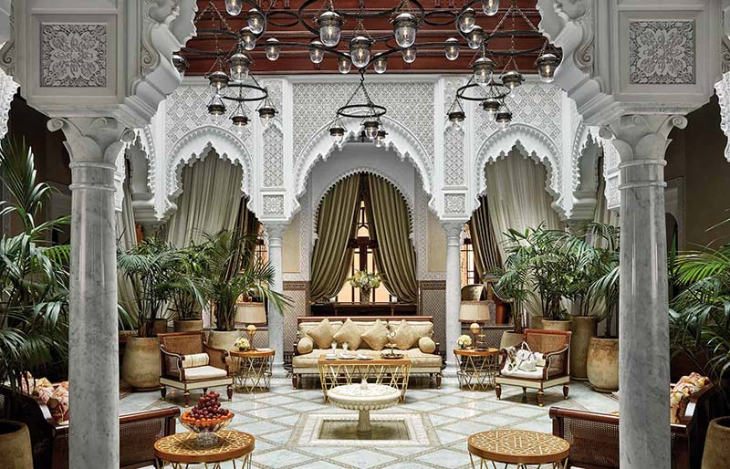 Luxurious Moroccan riad interior showcasing classical architecture with carved archways, opulent chandeliers, and a central garden area.