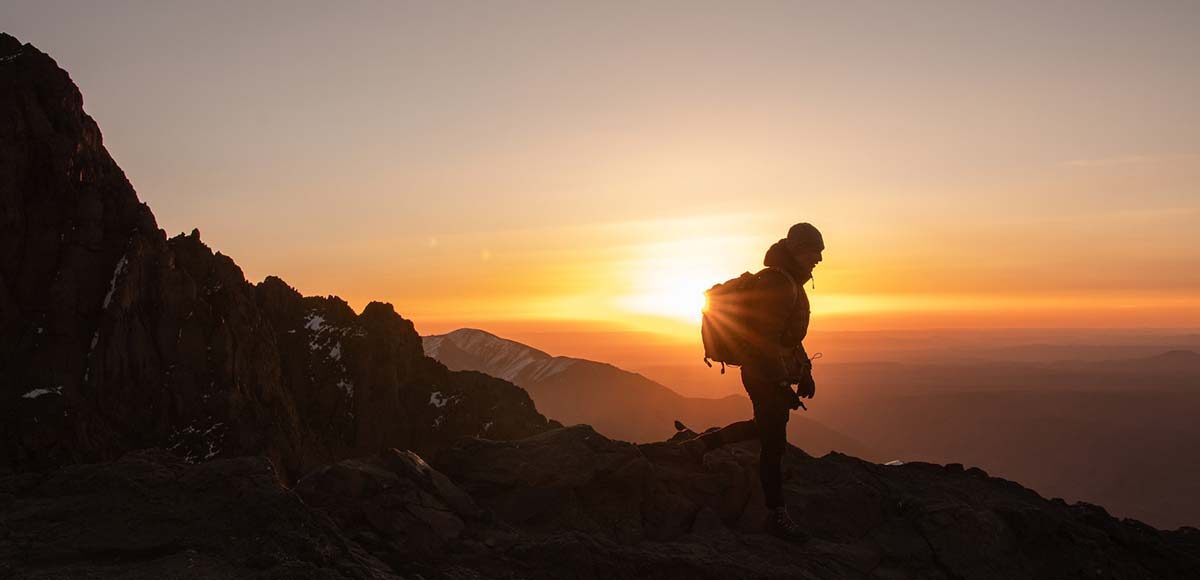 Hiker silhouetted at sunrise on a mountain ridge in the High Atlas Mountains, the gateway to the Sahara Desert.