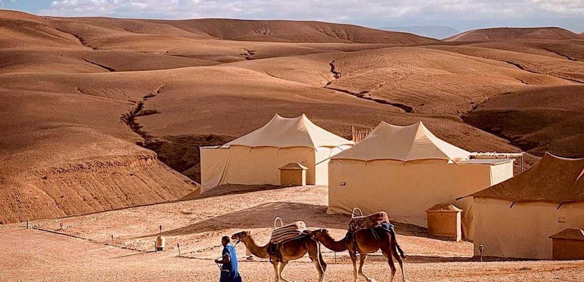 Camel caravan passing by luxury desert tents set among the rolling hills of Agafay.