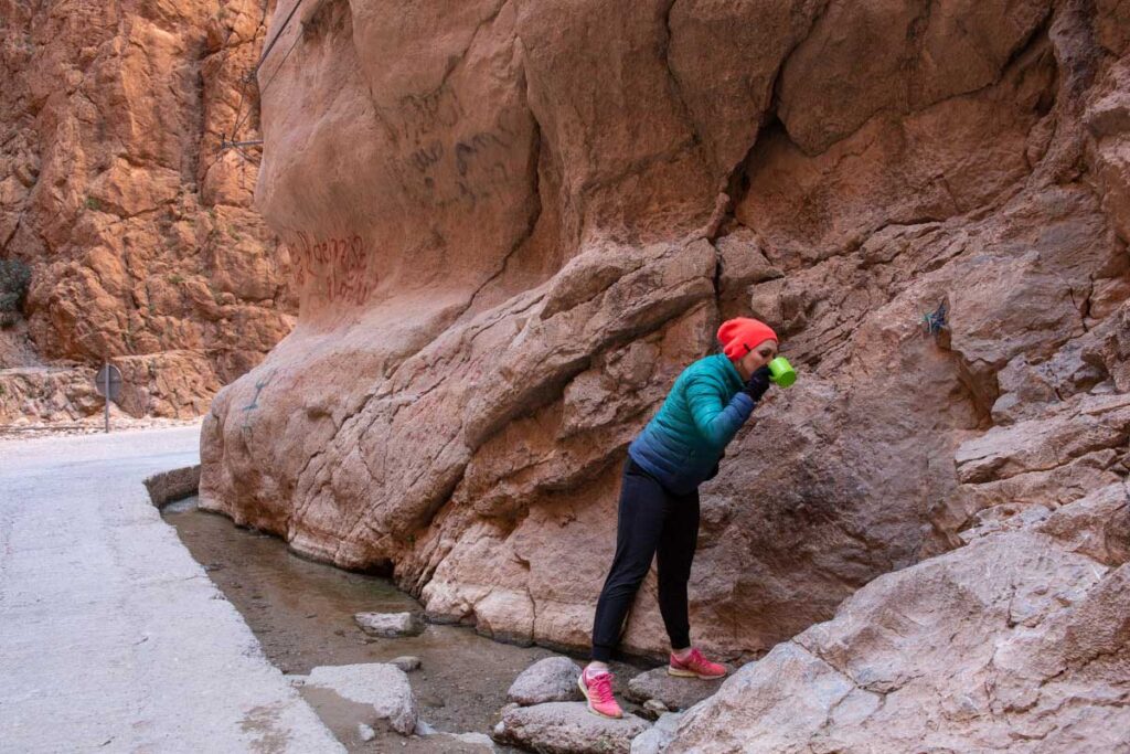 Visitor drinks crystal spring seep from Todgha Gorge wall on cool winter trek