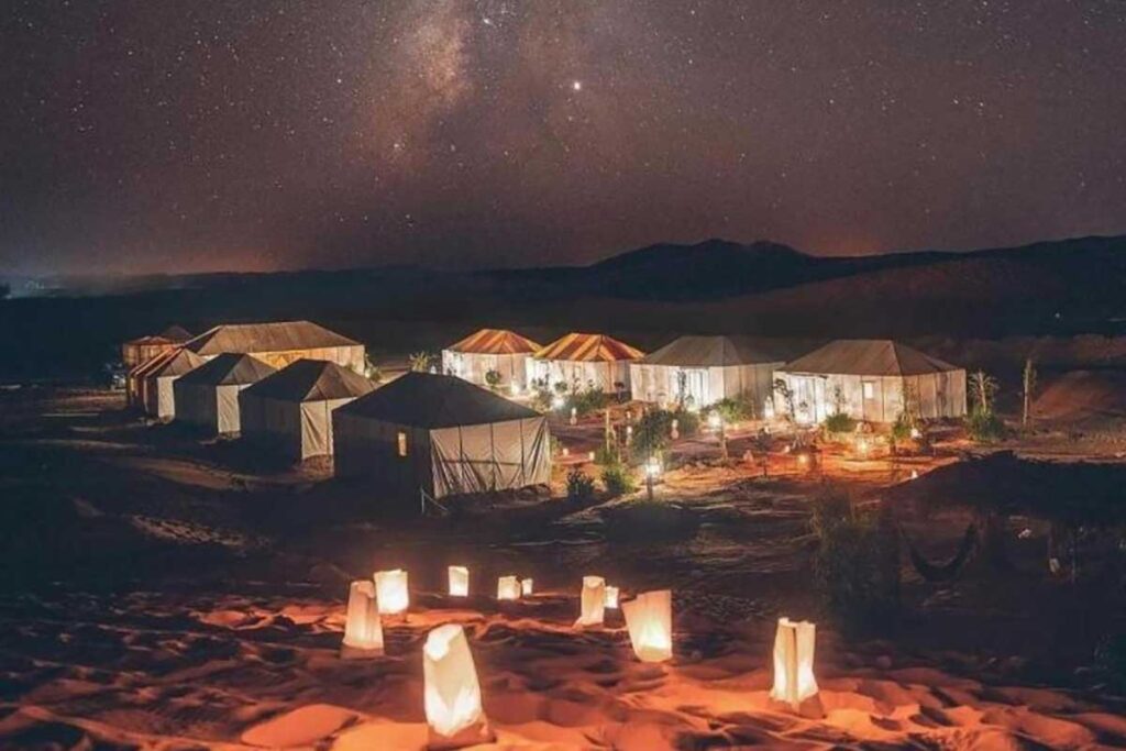 Luxury desert camp in Merzouga lit under the Milky Way night sky.