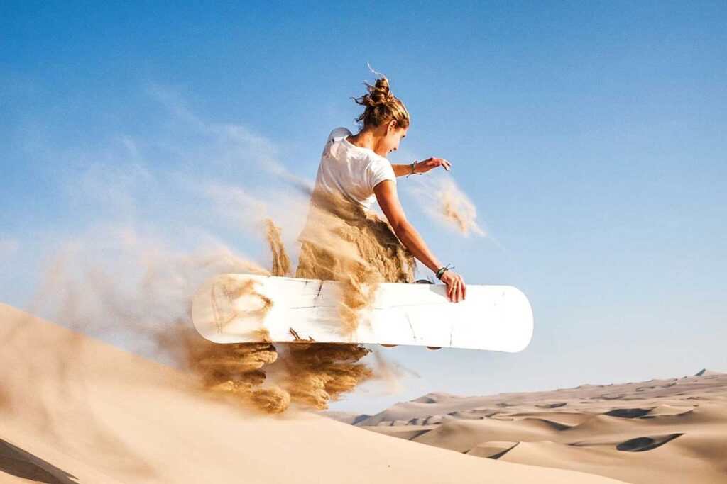 Traveler sandboarding down the golden dunes of Erg Chebbi in Merzouga.