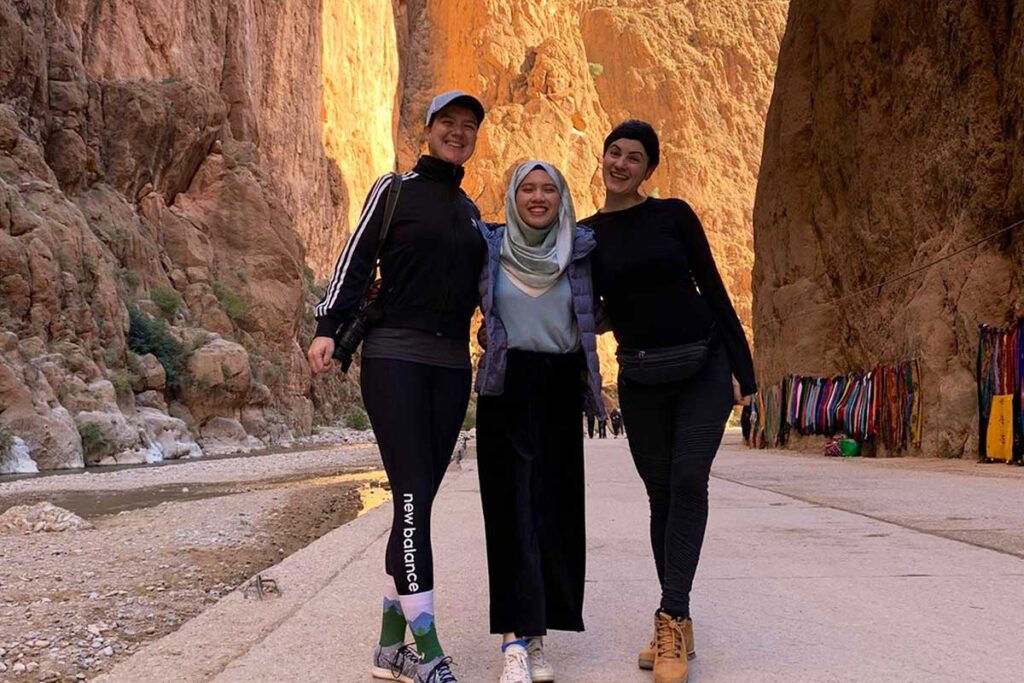 Three travellers pose beneath rose-gold Todgha Gorge cliffs on the river walkway