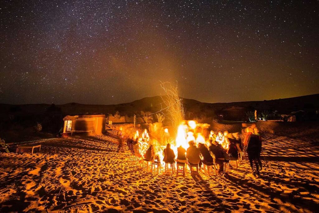Travelers around a campfire under a starry sky at a Zagora desert camp in Morocco.