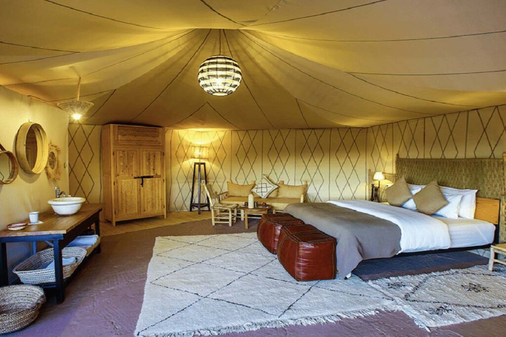 Interior of a Merzouga luxury desert camp tent with comfortable bed, seating area, and Moroccan decor