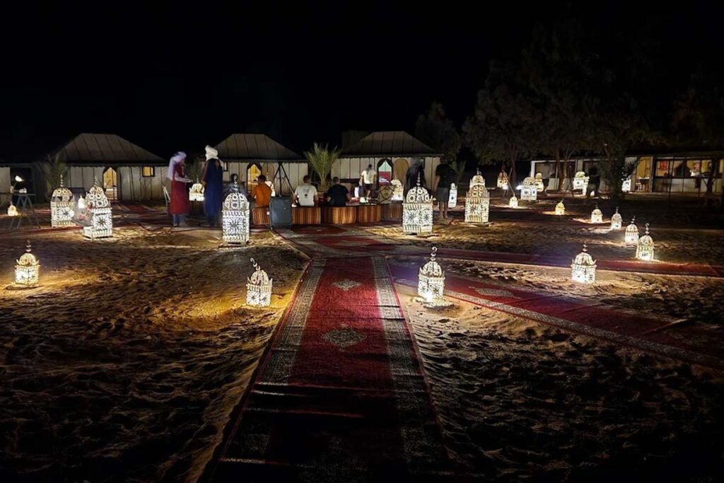 Lantern-lit walkway and seating area at night in a Merzouga luxury desert camp near the dunes