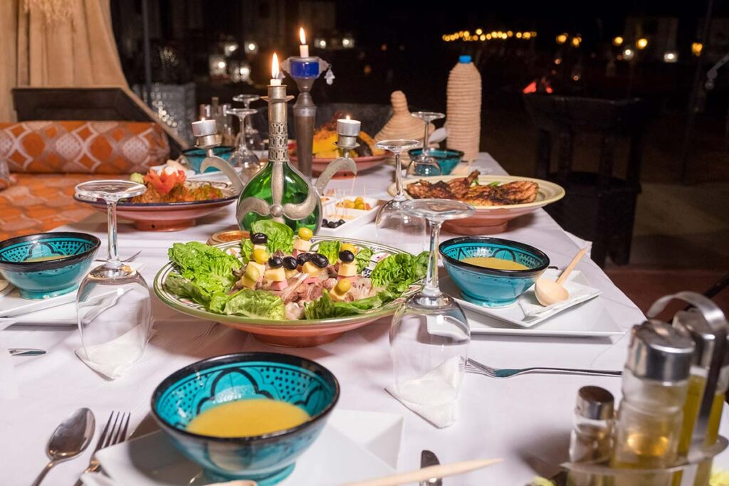 Traditional Moroccan dinner table set at a luxury desert camp in Merzouga with tajine and salads