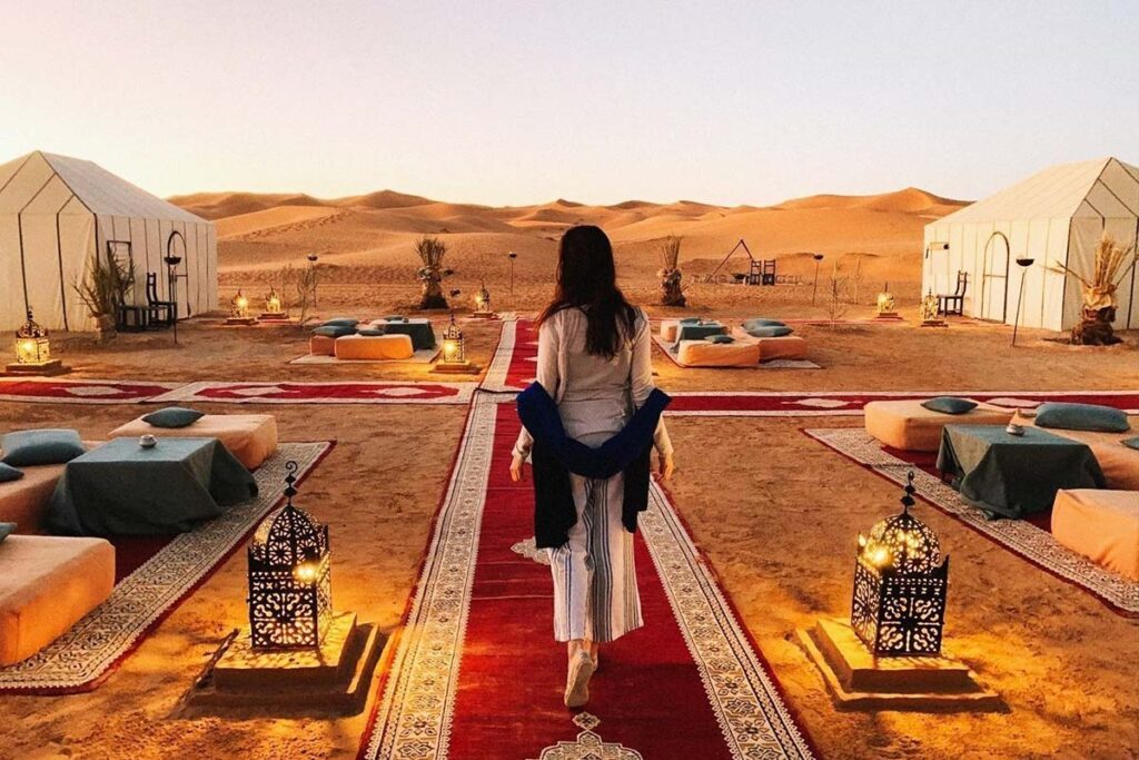 Guest arriving at sunset to a Merzouga luxury desert camp with lanterns and desert lounge setup