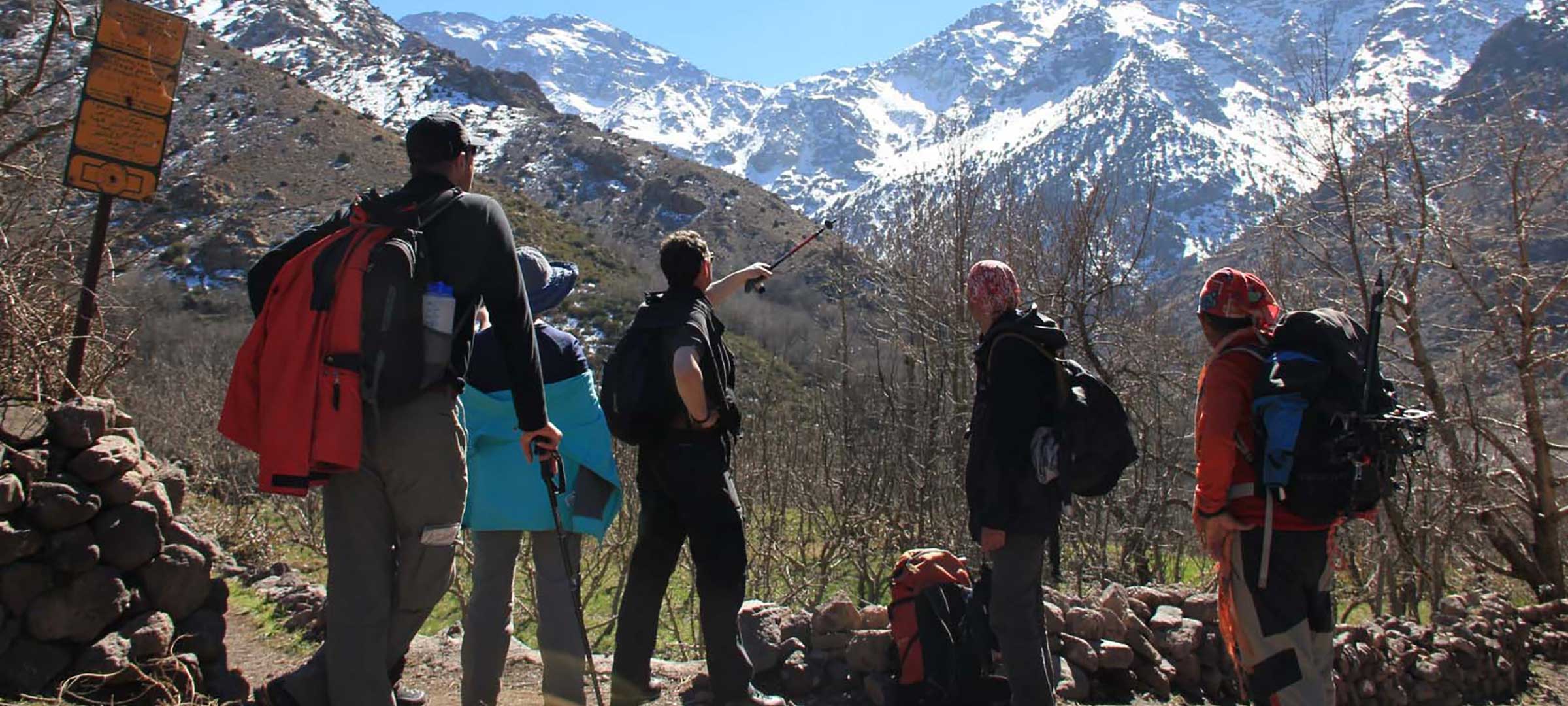 Trekkers on the 5-Day Toubkal Trek pausing on an Imlil Valley trail to view the snow-capped High Atlas summits