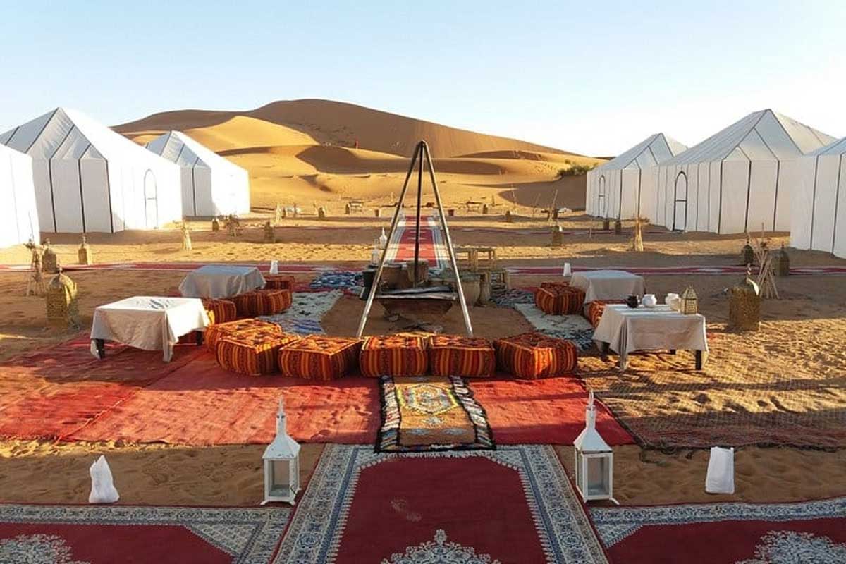 Luxury desert camp with white tents, Berber rugs and floor cushions set among the Erg Chebbi dunes near Merzouga on the 4-day Fes to Marrakech desert tour
