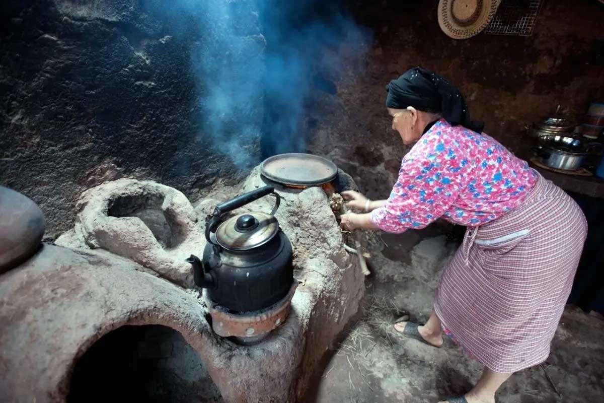 Berber woman preparing mint tea on a traditional clay stove inside a village home, Ourika Valley day trip from Marrakech