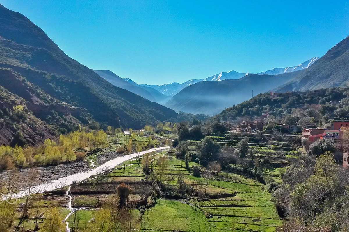 Panoramic view of the Ourika Valley with green terraced fields and misty High Atlas mountains, day trip from Marrakech